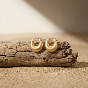 Gold earrings on driftwood and sand