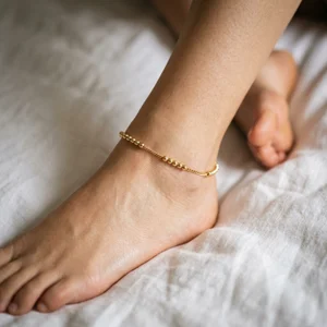 Dainty gold beaded anklet on sheets