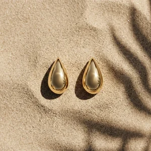 Gold earrings on sunny sand