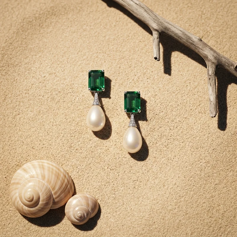 Emerald and pearl earrings on sand